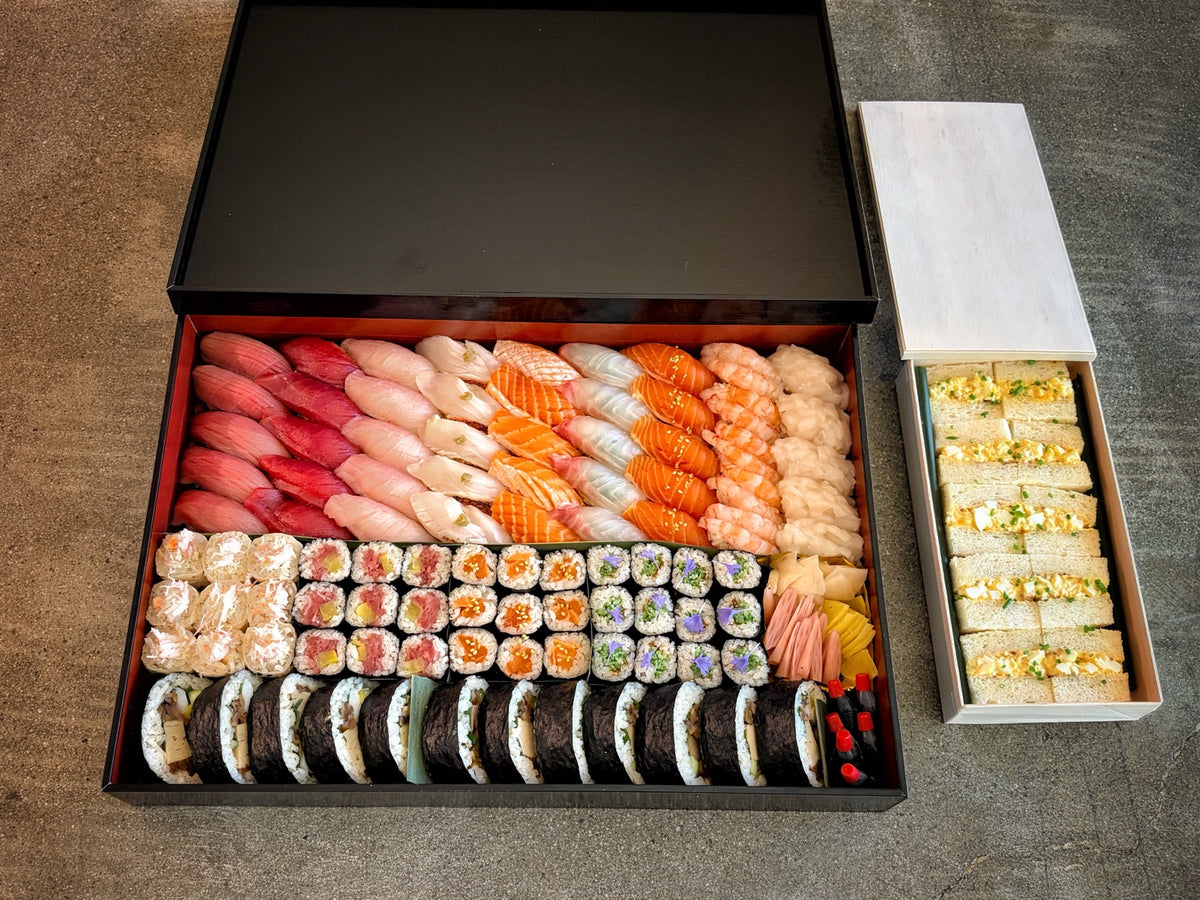 Kinkan Thanksgiving Party Tray in a black and red box with nigiri, assorted maki, futomaki, Japanese pickles and soy sauce, with egg sando in a separate wooden box.